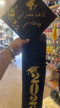 وشاح وقبعة تخرج مطرزة بعبارة أنا هنا بفضل أبي ودعاء أمي